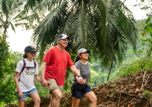Family of three smiling while walking through a forest