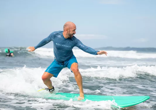Man smiling while standing on top of a surfboard