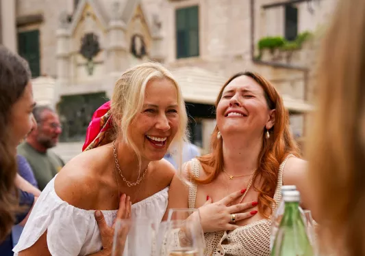 Two women smiling and laughing while drinking from glasses of wine