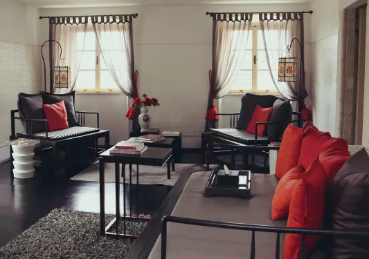 Three wooden chairs with pillows and cushions in a room with black floors and long curtains on the windows