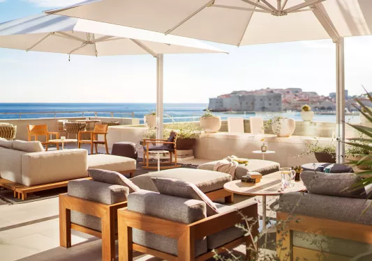 Outdoor patio with white umbrellas, with cushioned sofas and the ocean in the distance