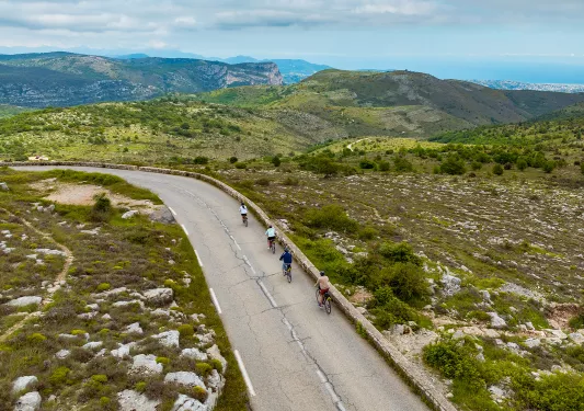 Group of people biking on an empty road, surrounded by a grassy valley
