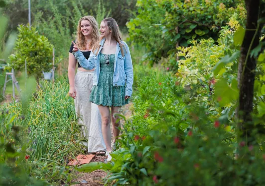Two women walking through a garden, pointing and smiling