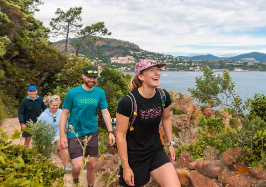 Group of people smiling while hiking on a trail with the ocean in the background