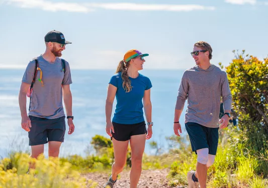Two men and one woman hiking on a trail with the ocean in the background