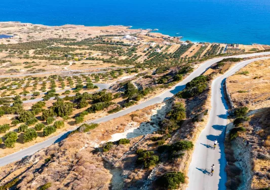 Long, empty roads with people biking, with the ocean in the distance