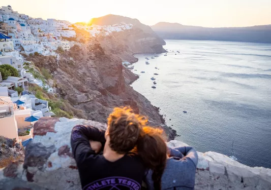Man and woman leaning their heads on their shoulders, looking out to a large cliff full of houses