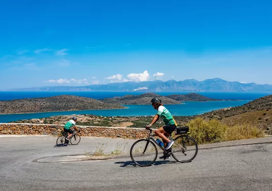 Two people riding bikes down a road, with a large lake in the distance