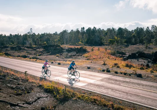 Two people riding a bike on an empty road with a forest in the background