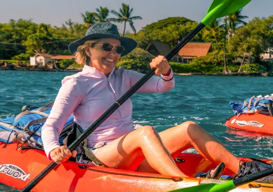 Woman wearing a hat and sunglasses, paddling on an orange kayak