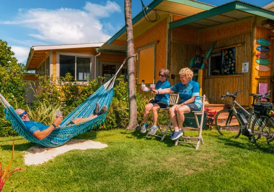 Man laying down on a hammock with two women sitting on wooden stools next to him