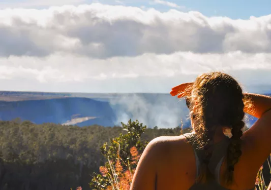 Woman using their hand as a sun visor, looking out to a tall forest