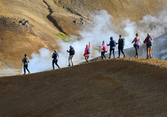 Group of people walking along a dirt trail on a hill, with fog in the background
