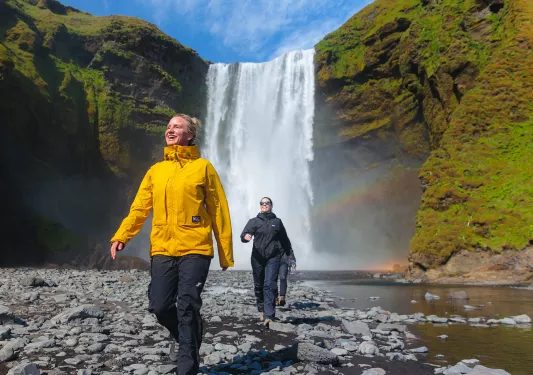 Two women smiling while walking on a rocky path in front of a waterfall