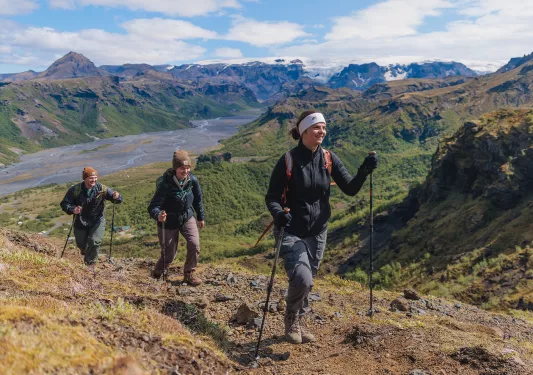 Group of three people with hiking poles, walking on a dirt and gravel trail on a hill