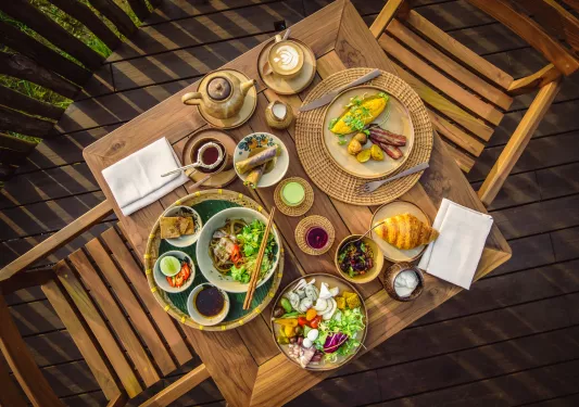 Top-down view of restaurant table full of plates of colorful food and two wooden chairs