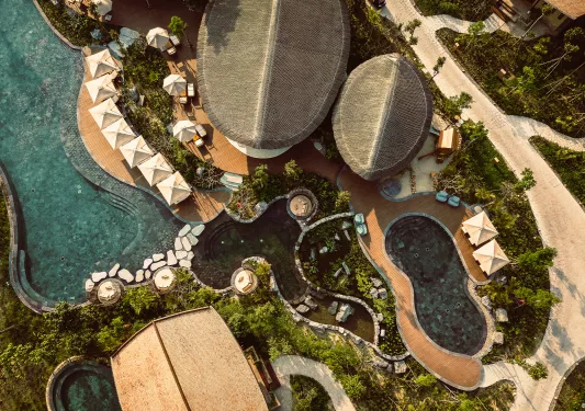 Top-down view of an outdoor pool and gray villas, with sandy paths along the sides