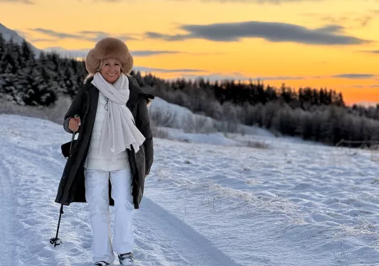 Woman in snow gear and walking poles walking through a snowy trail