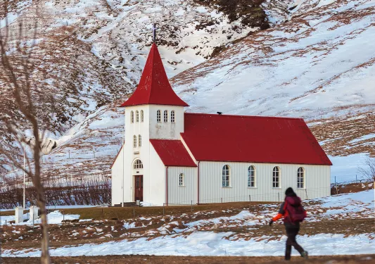 Person walking on a dirt path with a red and white church in the background