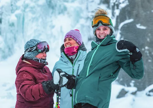 Three women wearing warm snow jackets and mittens while laughing