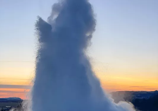 Active geyser in the middle of a valley with the sunset in the background