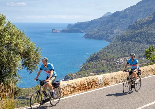 Two people riding their bikes on a road, with the ocean in the distance