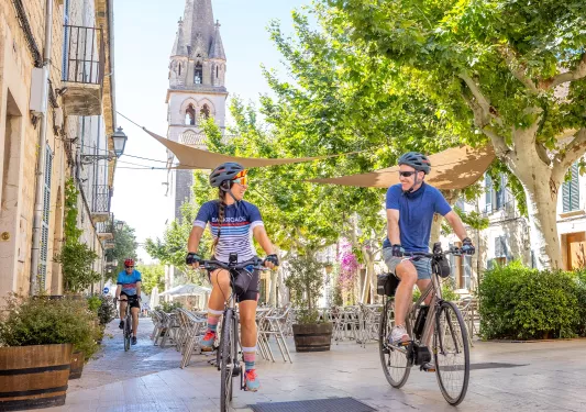 Man and woman riding their bike on an alleyway with a church bell tower view in the distance