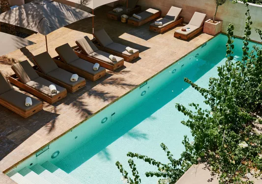 Outdoor pool surrounded by reclining green chairs and gray umbrellas