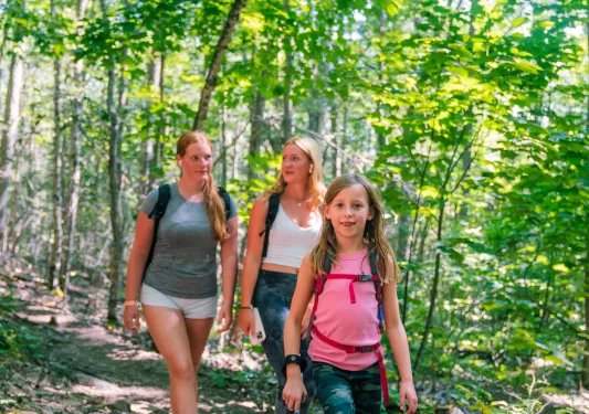 Group of two women and one child walking through a forest with tall, green trees