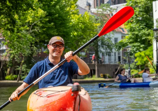 Man smiling while paddling in a red kayak on a river