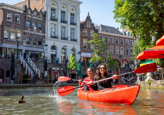 Two women paddling in a red kayak with a European town in the background