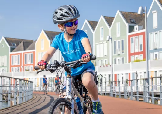 Boy smiling while riding a bike on a bridge, with rows of colorful houses in the background
