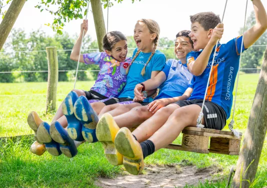 Group of kids smiling and laughing, while sitting and swinging on a wooden swing