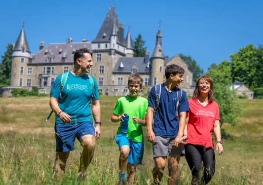 Family smiling while walking through a grassy field, with a castle-like building in the background