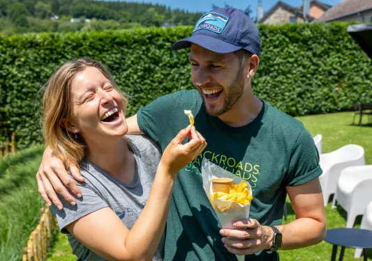 Man and woman smiling with their arms around their shoulders, holding a cone of fried potatoes