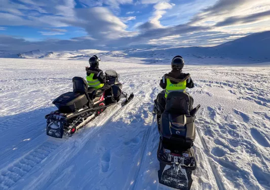 Two people riding on snow mobiles in a vast valley of snow