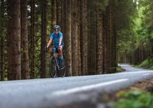 Woman riding a bike on a road, surrounded by a forest