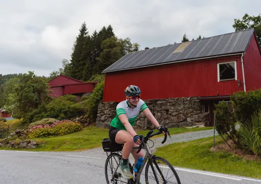 Person smiling while riding a bike in front of a red house