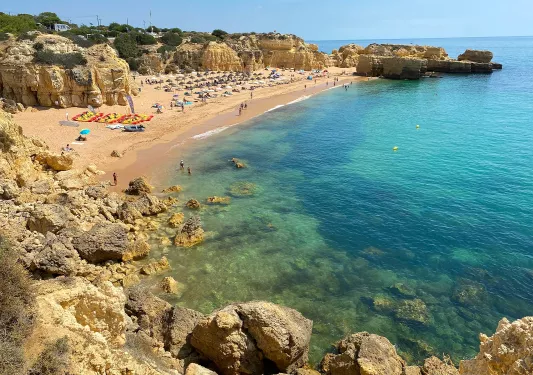 Group of people sitting by the beach, with large cliffs surrounding the area