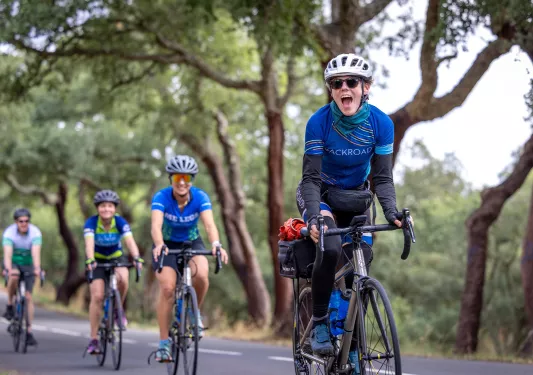 Group of people riding bikes on an empty road, surrounded by tall trees