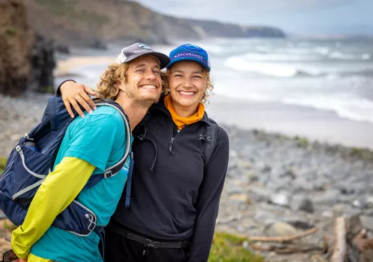 Man and woman smiling and hugging in front of a beach