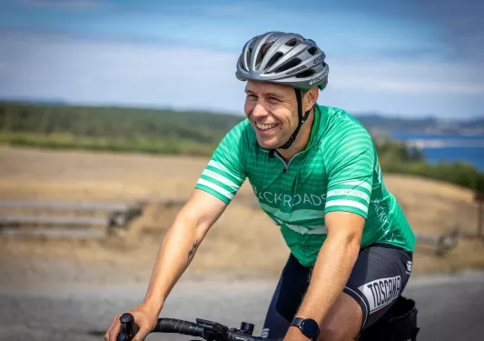 Man wearing green biking gear, smiling while biking on an empty road