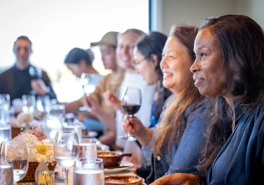 Group of people eating at a dining table while holding their glasses of wine