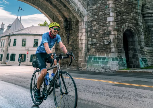 Man riding a bike on a road under a stone arc in a city