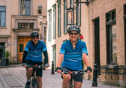 Man and woman riding their bikes along a stone alleyway in a town