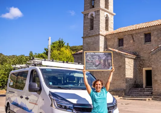 Woman smiling, holding up a chalkboard in front of a white van