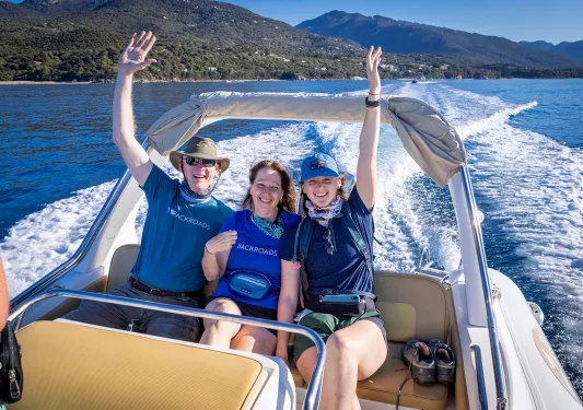 Three Backroads guests put their hands in the air on the back of a boat
