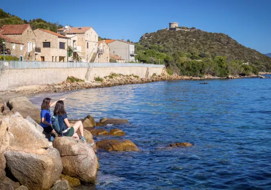 Two women sitting on a large boulder next to the ocean