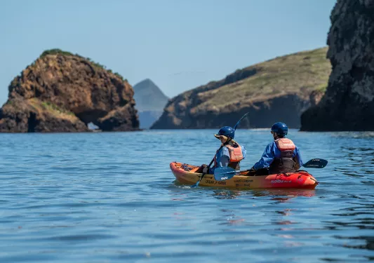 Two people on an orange and yellow kayak, paddling in the middle of the ocean