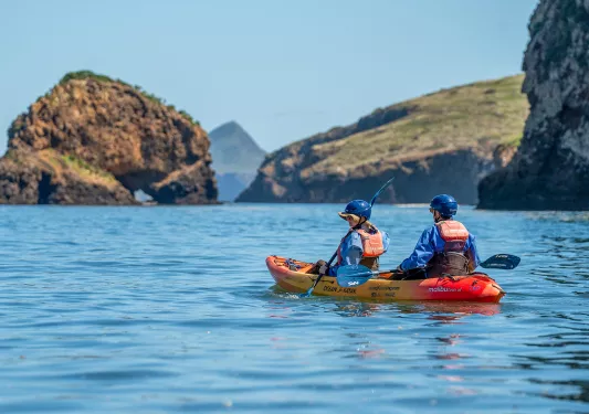 Two people paddling on an orange kayak in the middle of a lake